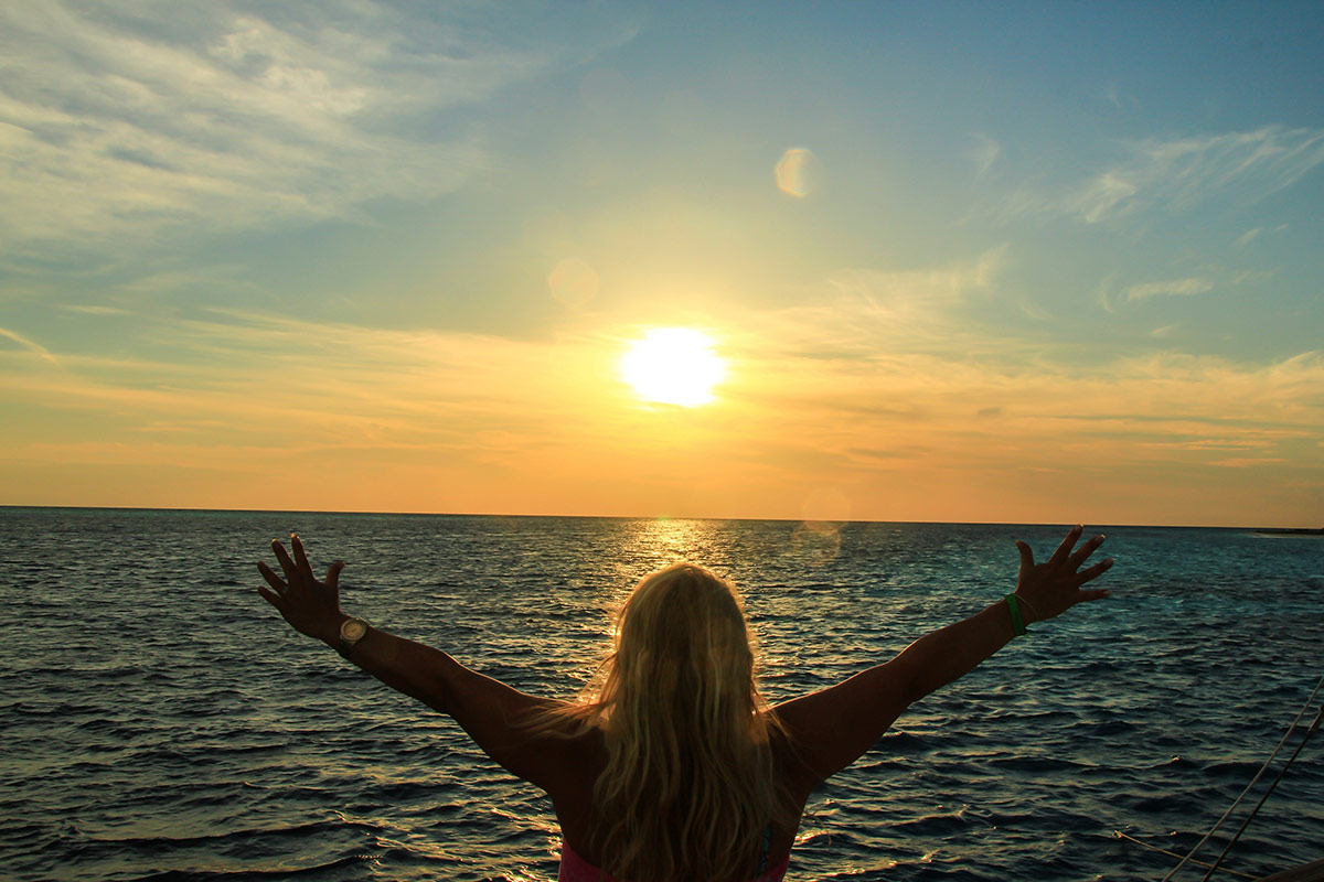 a woman holding her hands out as she looks at the sun over water